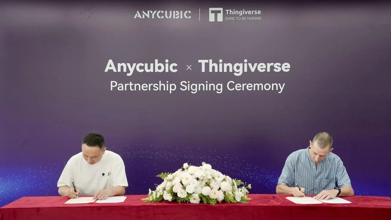 An Anycubic representative and a Thingiverse representative signing papers at a table under an "Anycubic x Thingiverse Partnership Signing Ceremony" banner